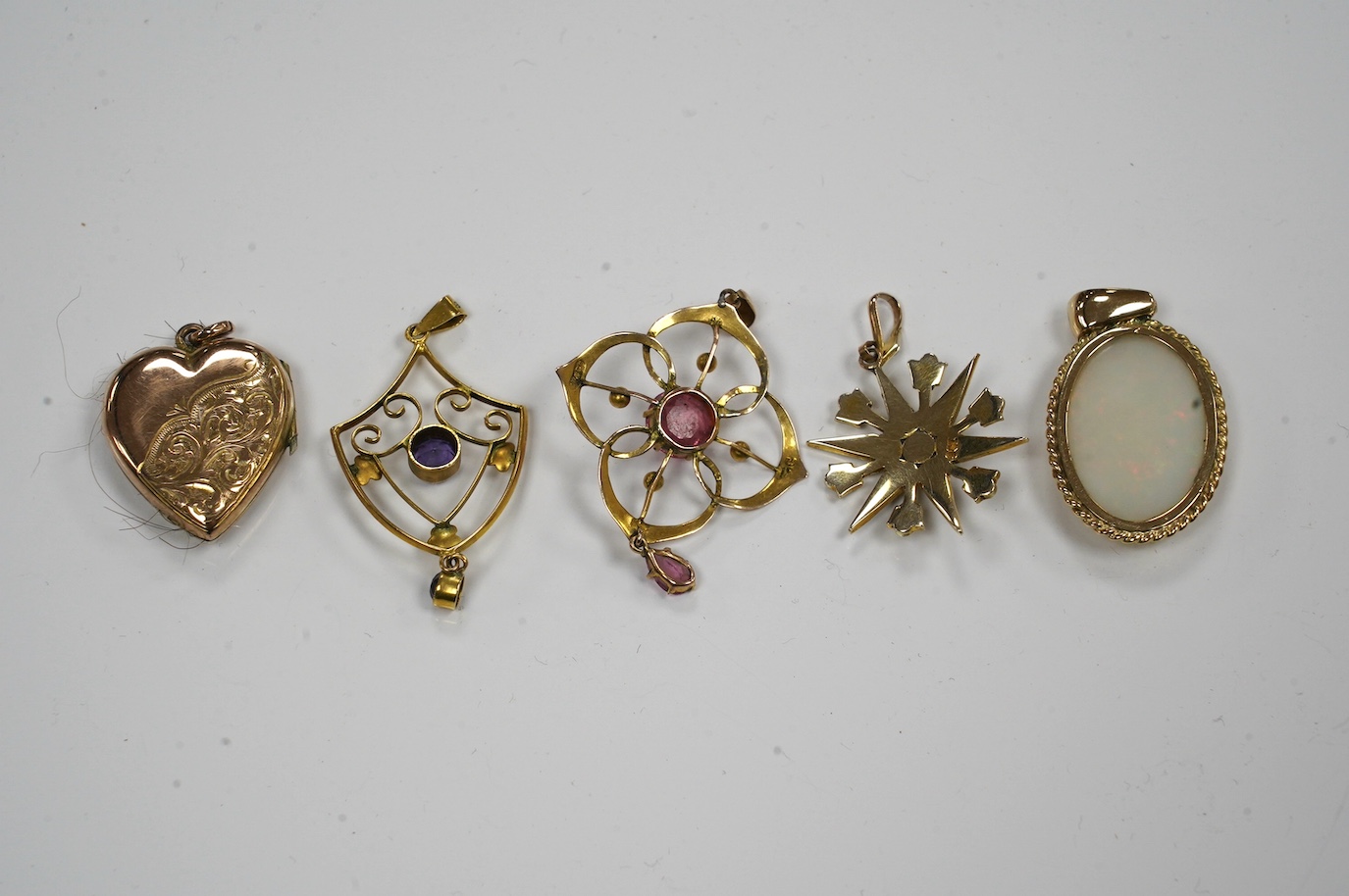 Five assorted gem set pendants including a 9ct and seed pearl star, 20mm, a yellow metal and amethyst set drop, a yellow metal and white opal and an Edwardian yellow metal heart shaped locket. Condition - fair
